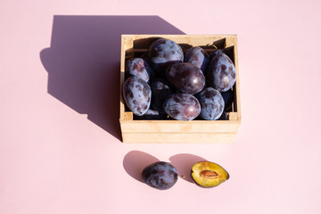fresh blue plums in wooden box on pink background, top view