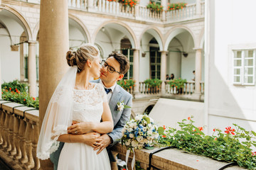 Exquisite couple standing on the balcony. Italian architecture. Husband kisses his wife on the cheek