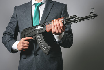 Businessman with a assault rifle airgun on a gray background. Business protection. Threat to...