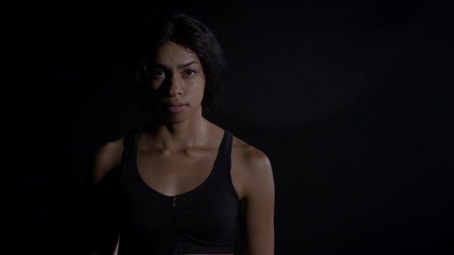 MS mixed race woman walks forward from soft focus against black background. She comes into focus, looking at camera and nods HD