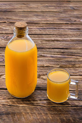 Fresh orange juice in bottle and mug on wooden table