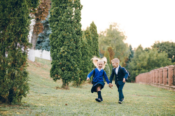 little boy and girl after school lessons joyfully run on the green lawn. Back to school. Cute kids with backpacks on their back running to school having fun.