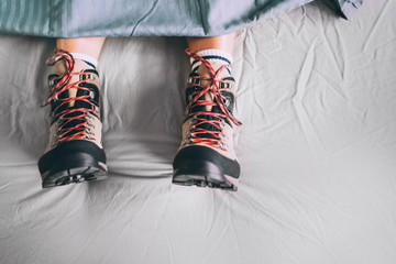 All time ready for trekking. Hiker sleeping in comfort trekking boots. Footwear on the bed sheet background concept image.