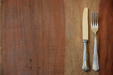 Background from a table top of a rustic wooden table on which lie an old decorated fork and an old decorated knife