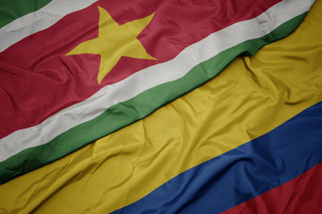 waving colorful flag of colombia and national flag of suriname.