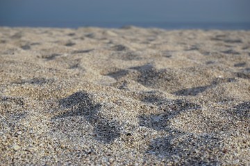 Close-up view of sand and pebbles on beach with blurred sea background.
