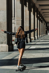 Beautiful young skater woman riding on her longboard in the city. Stylish girl in street clothes rides on a longboard.