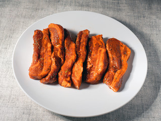 Fresh uncooked pork belly slices in Korean style marinate on a white plate.