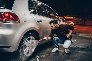 Young man washing his car in the evening at car wash station.