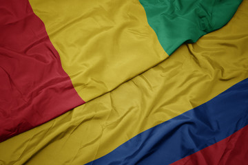 waving colorful flag of colombia and national flag of guinea.