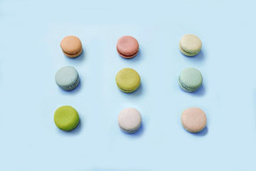 Top view of sweet macaroon biscuits lying in three lines on light blue background.