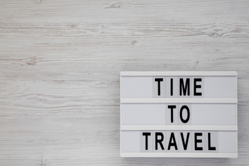 'Time to travel' words on a modern board on a white wooden background, top view. Overhead, from above, flat lay. Copy space.