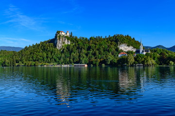 Fototapeta na wymiar Beautiful view of the shore of Lake Bled with a medieval castle and the Catholic Church of St. Martin.