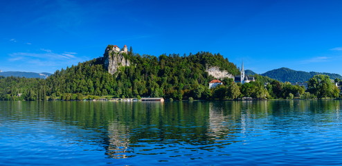 Fototapeta na wymiar Beautiful panoramic view of the shore of Lake Bled with a medieval castle and the Catholic Church of St. Martin.