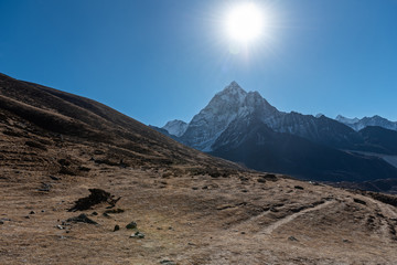 The dry winter brings out brown colours that cover the hilly landscape with tall sharp mountains in the background on a clear sunny day in the Nepalese Himalayas