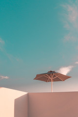Obraz na płótnie Canvas Sun parasol on a white washed balcony against blue sky. Minimal Architecture of Mykonos, Santorini and the Cyclades. 
