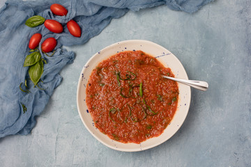 Homemade Chunky Tomato Soup on Textured Blue Background with Tomatoes and Basil in Background