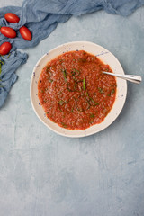 Homemade Chunky Tomato Soup on Textured Blue Background with Tomatoes and Basil in Background