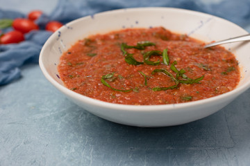 Homemade Chunky Tomato Soup on Textured Blue Background with Tomatoes and Basil in Background