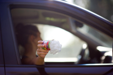 Girl holds trash outside the car window. A woman is about to throw waste out of a car....