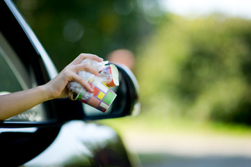 Girl holds trash outside the car window. A woman is about to throw waste out of a car. Environmental pollution, selective focus, backlight