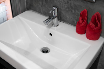 Modern stainless steel faucet with wash basin sink with a two red towels on it . Counter bathroom interior contemporary. Luxury and stylish design bathroom with a concrete style walls.
