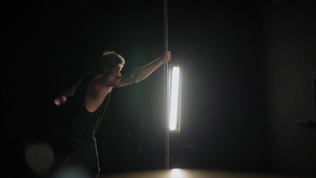 The guy shows the exercise on a pole.. Male pole dance. Photo of muscular man posing