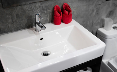 Modern stainless steel faucet with wash basin sink with a two red towels on it . Counter bathroom interior contemporary. Luxury and stylish design bathroom with a concrete style walls.