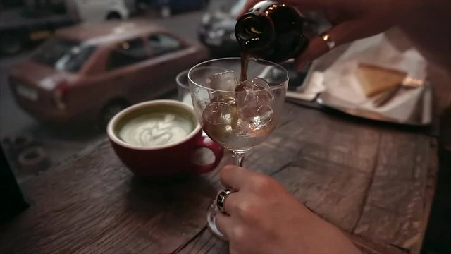 Girl pours cold brew coffee in a glass of ice in a cafe in the evening.