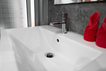 Modern stainless steel faucet with wash basin sink with a two red towels on it . Counter bathroom interior contemporary. Luxury and stylish design bathroom with a concrete style walls.