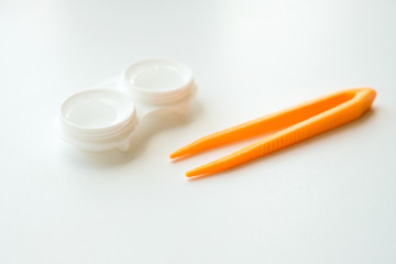 Accessories for the proper use of contact lenses: case and orange tweezers on light white background. Safe vision correction. Selective focus.