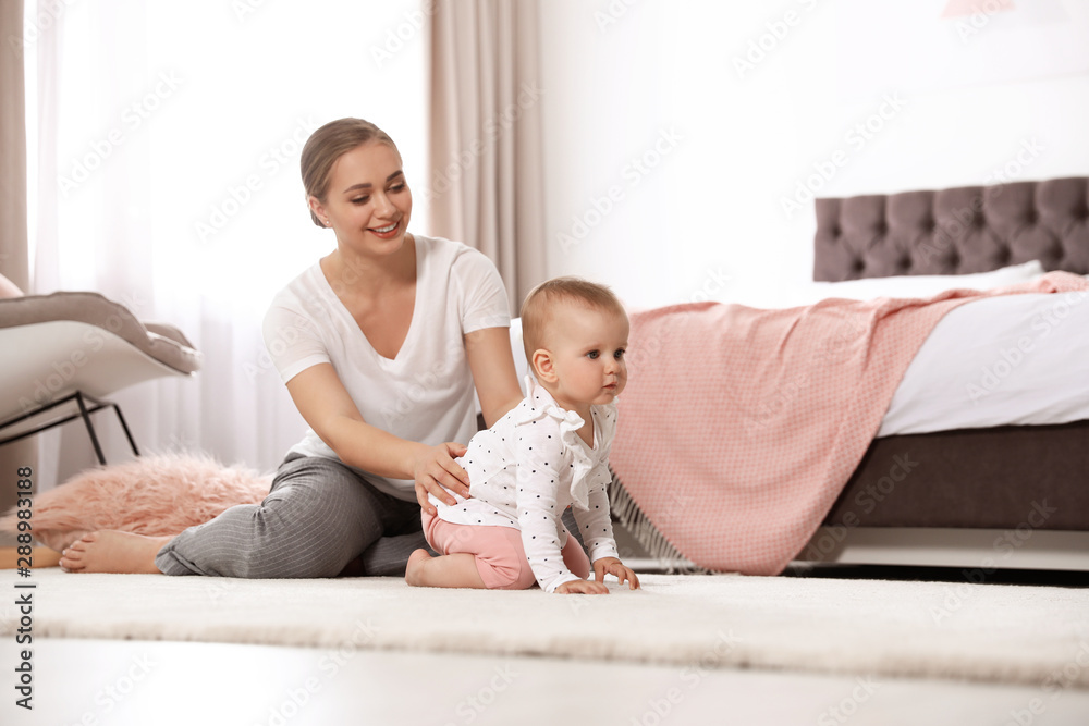 Wall mural Mother watching her baby crawl on floor in bedroom