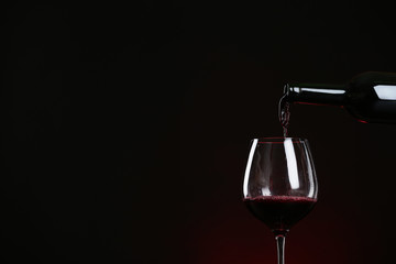 Pouring wine from bottle into glass on dark background, space for text