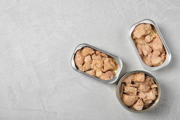 Open tin cans with tuna and cod liver on grey table, flat lay. Space for text
