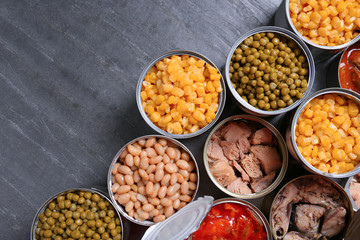 Open tin cans of conserved products on grey table, flat lay with space for text