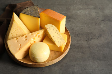 Wooden plate with different sorts of cheese on grey table, space for text