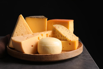 Wooden plate with different sorts of cheese on grey table against black background