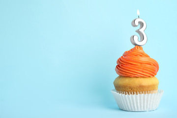 Birthday cupcake with number three candle on blue background, space for text