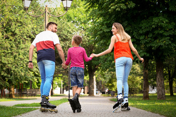 Fototapeta premium Young family roller skating in park, back view