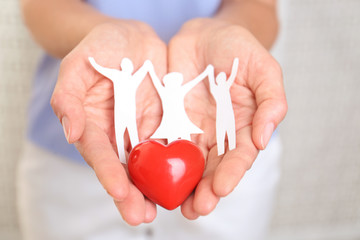 Young woman holding paper family figure and red heart, closeup of hands