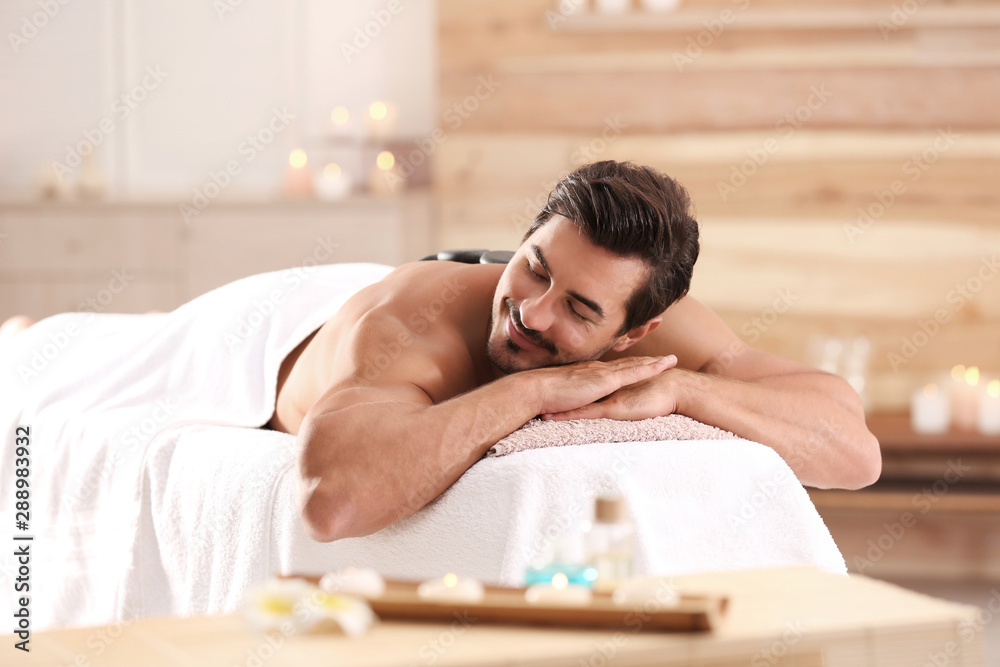 Poster Handsome young man receiving hot stone massage in spa salon