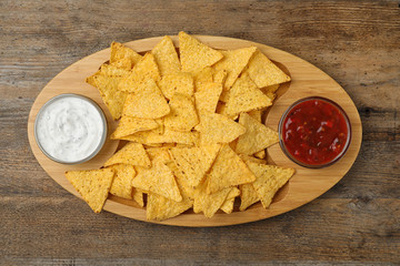 Mexican nacho chips with different sauces on wooden background, top view