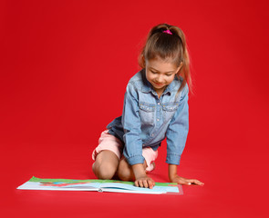 Naklejka premium Cute little girl reading book on red background