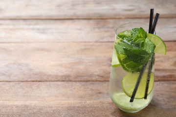 Glass of tasty refreshing cocktail with lime and mint on wooden table. Space for text