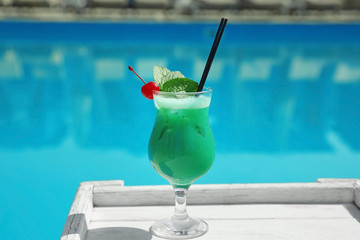 Refreshing cocktail on wooden table near swimming pool outdoors