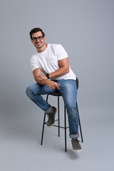 Handsome young man sitting on stool against grey background