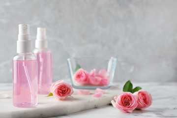 Fototapeta na wymiar Bottles with rose essential oil and flowers on marble table, space for text