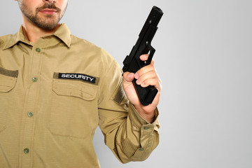 Male security guard in uniform with gun on grey background, closeup. Space for text