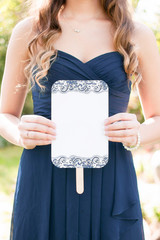 young bridesmaid wearing a navy dress and long hair holding a blank wedding ceremony program fan, wedding itinerary, copyspace, blank card
