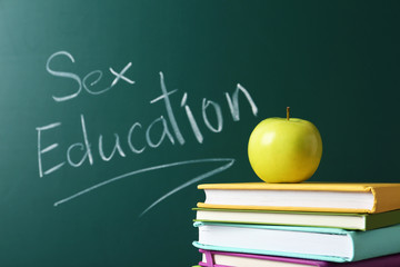 Books and apple near chalkboard with phrase "Sex education"